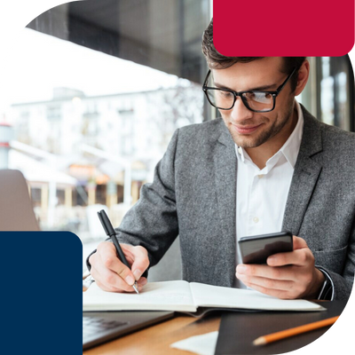 Ameripol-FinancialManager-man-sitting-infrontof-computer-writing-a-pen-with-mobile-in-his-hand